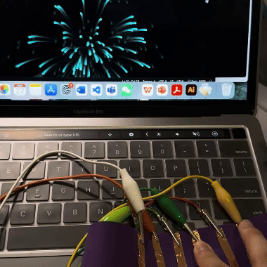In a demonstration, I touch the copper strips connected to the Makey Makey board, and each touch triggers a beautiful fireworks display on my computer screen. This shows how physical actions can interact with digital applications in real time.